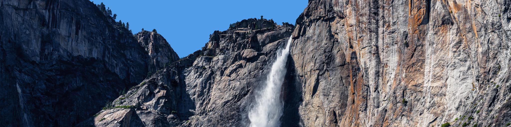 Crashing waters falling from Lower Yosemite Waterfall, with bright blue skies in background