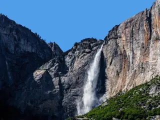 Crashing waters falling from Lower Yosemite Waterfall, with bright blue skies in background