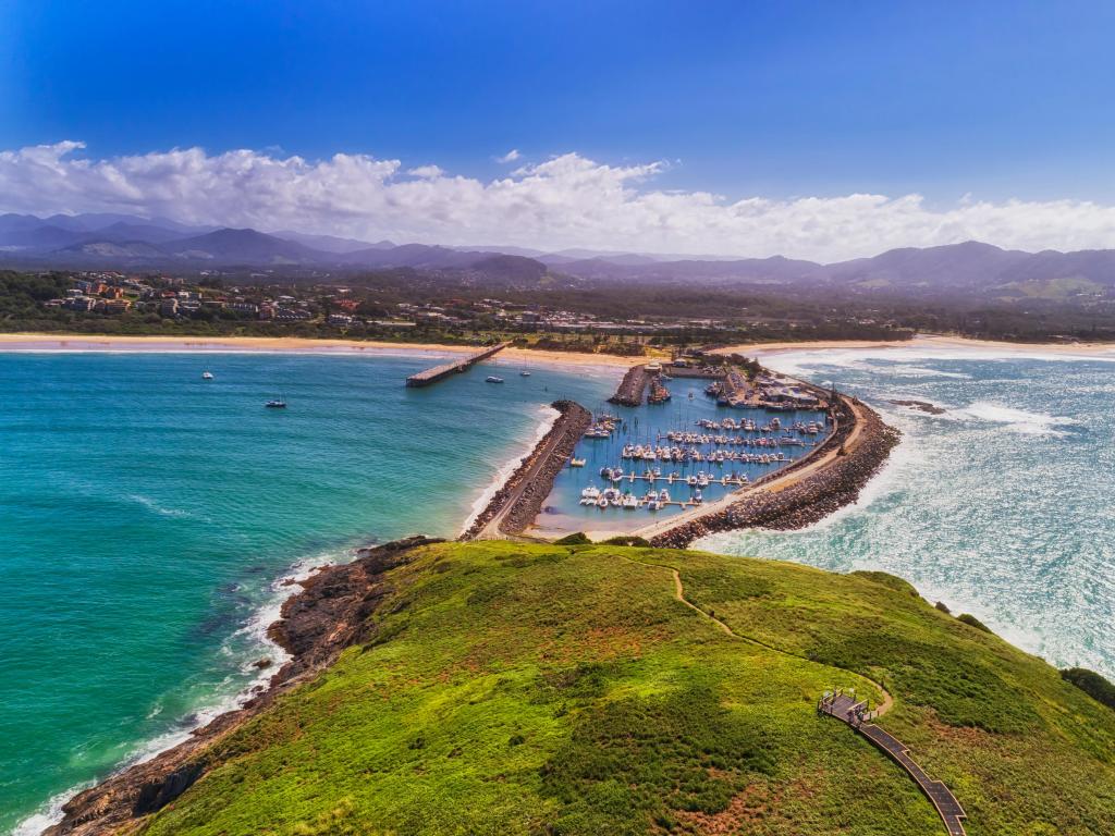 Coffs Harbour, Australia looking at the town from Muttonbird Island connected to shore by stone walls, protecting the marina and a sandy beach in the distance.