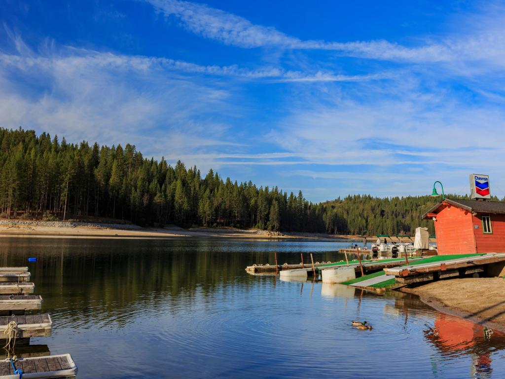 A red wooden hut stands on the shores of Bass Lake in Madera County, California, with a boat ramp leading down to the water