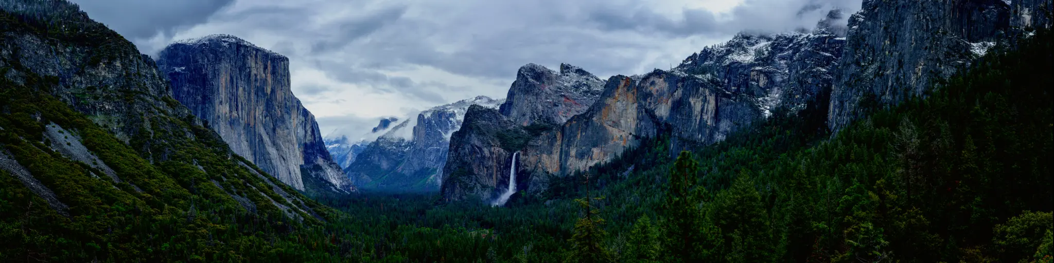 A breathtaking view of Rock formations, waterfall, and pine trees in Yosemite National Park on a gloomy afternoon