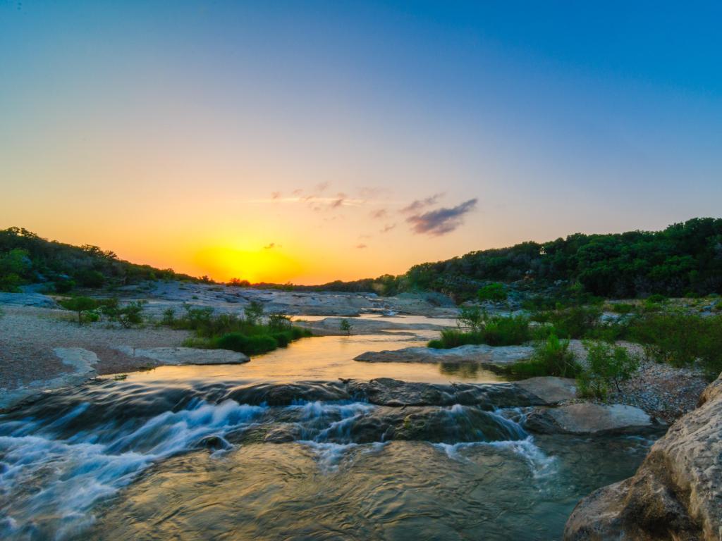 Sunset over a rocky but calm river with small waterfall in the foreground