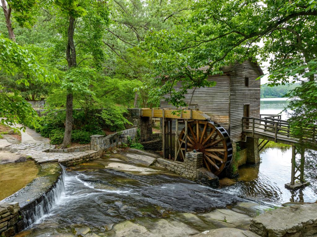 Old wooden water mill by lake with green trees