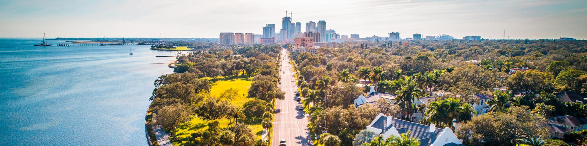 St Petersburg, Florida with a road running alongside the ocean with the city in the background on a sunny day. 