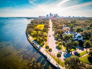 St Petersburg, Florida with a road running alongside the ocean with the city in the background on a sunny day. 