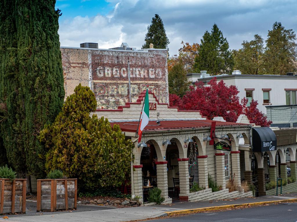 A historic red and cream brick building stands on Main Street in Ashland, Oregon, with faded lettering on its facade
