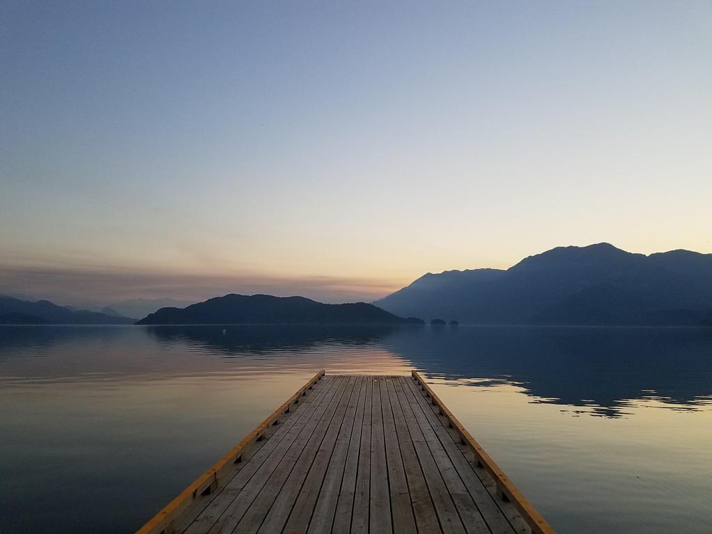 A wooden jetty leading out onto a tranquil lake at dusk