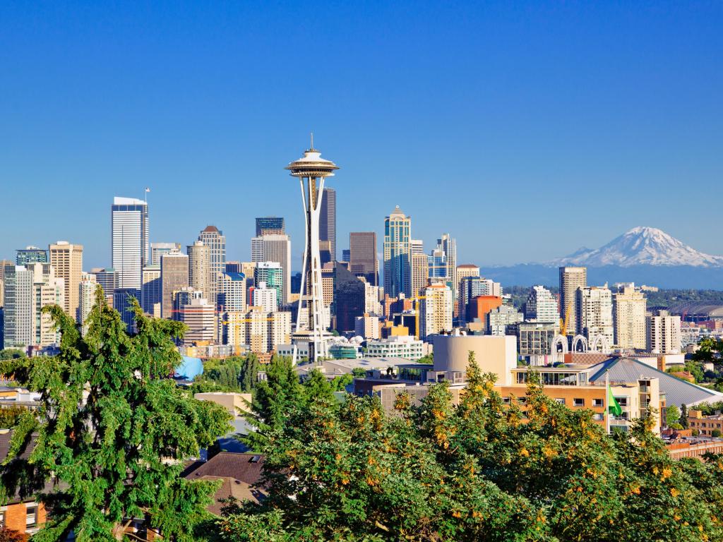 Seattle, USA with the city skyline and trees in the foreground and Mount Rainier in the distance on a clear day.