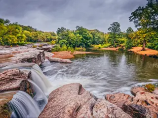 McKinney Falls State Park, Austin with a creek spilling water and trees surrounding the water and rocks in the background.