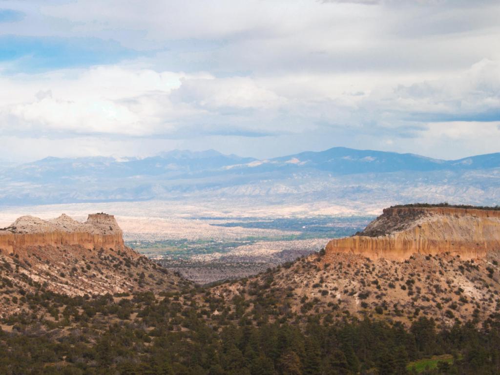 Los Alamos, New Mexico, USA with clouds form patterned layers above plateaus near Los Alamos, trees lining the foreground and mountains in the background.