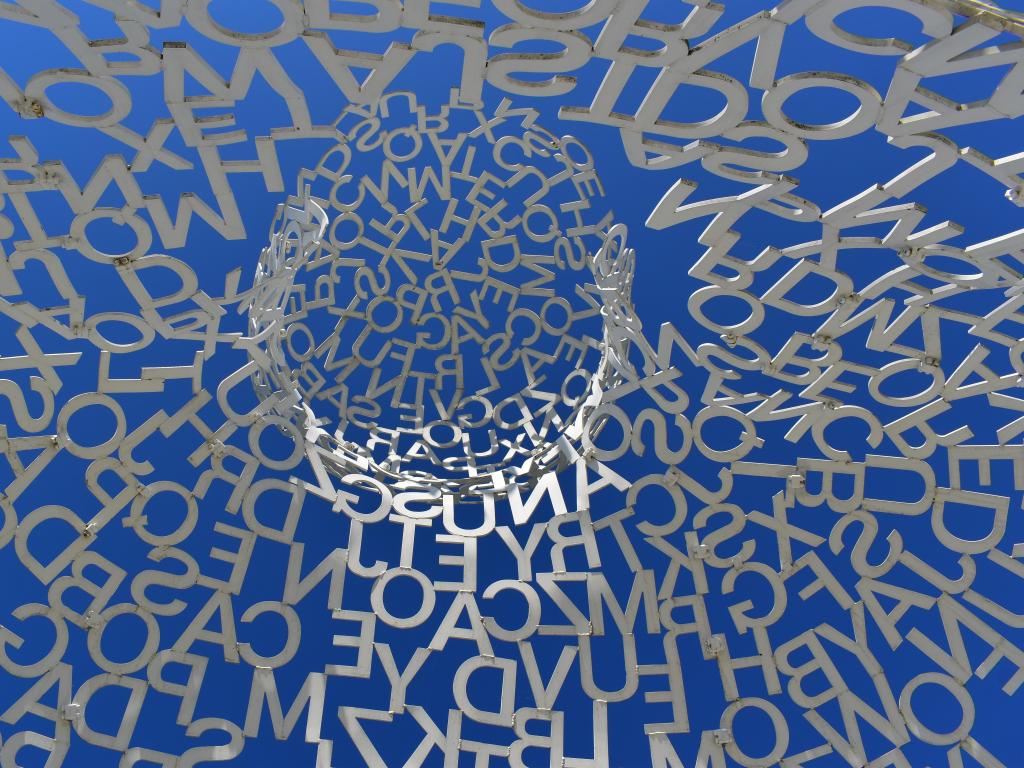 View from within a sculpture looking up at the blue sky through a dome of metal letters at Pappajohn Sculpture Park, Des Moines