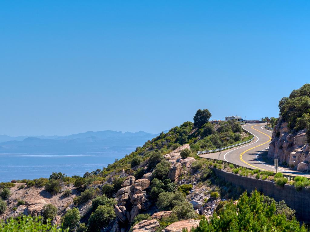 A winding road along the side of a mountain with rocks and greenery, with a far reaching view