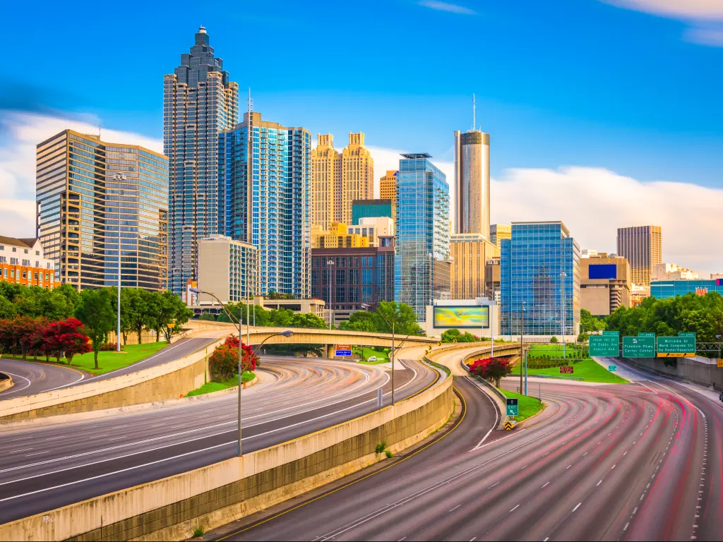 A long exposure shot of Interstate 85 with trees of red and green along the highway and the skyline of downtown Atlanta, Georgia in a sunny morning