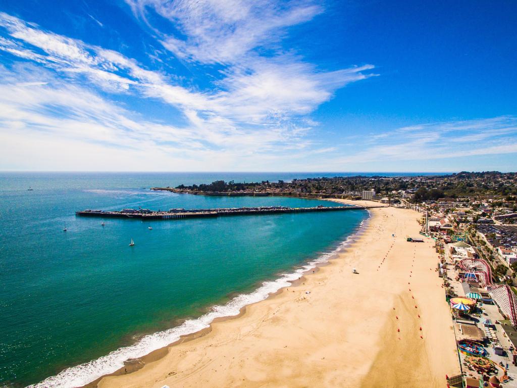 Santa Cruz Beach on a clear sunny day with a long stretch of sand and rides in the background.