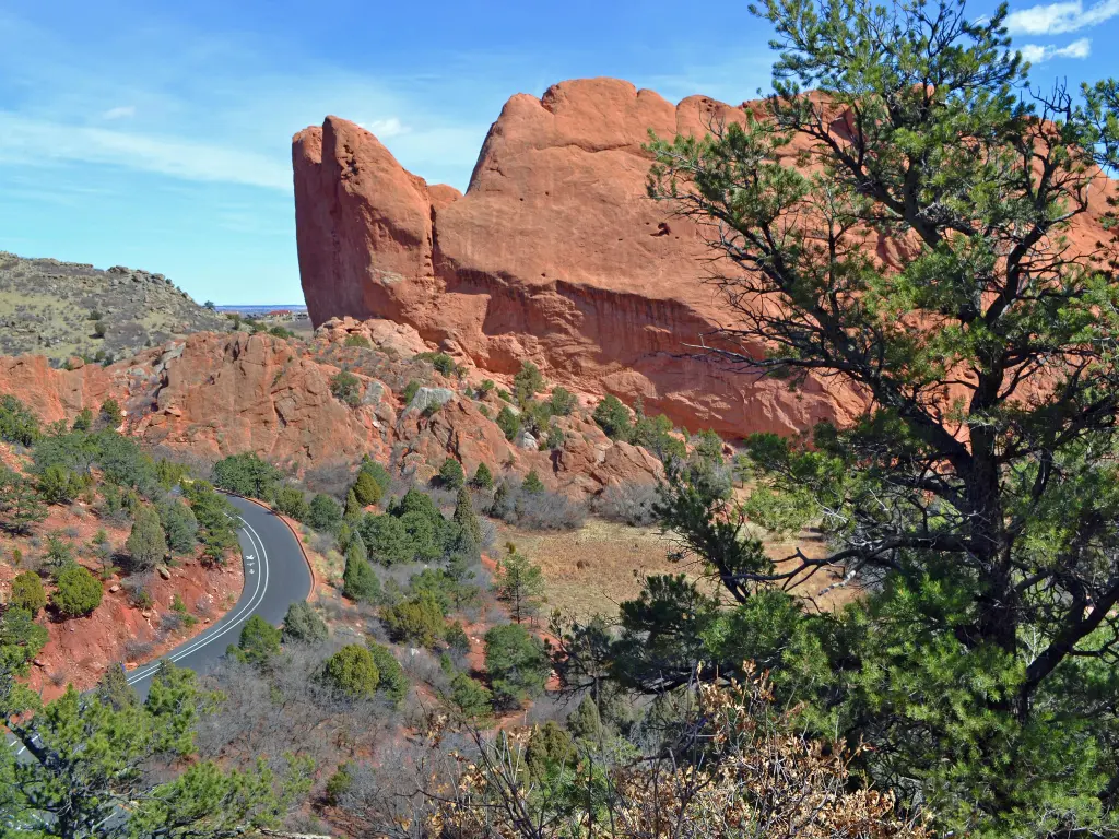 Red rocks tower over a road winding through the park and shrubbery in Garden of The Gods, Colorado