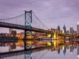 The Delaware River mirrors the Ben Franklin Bridge and the Philadelphia skyline, all under the hues of a purple twilight.