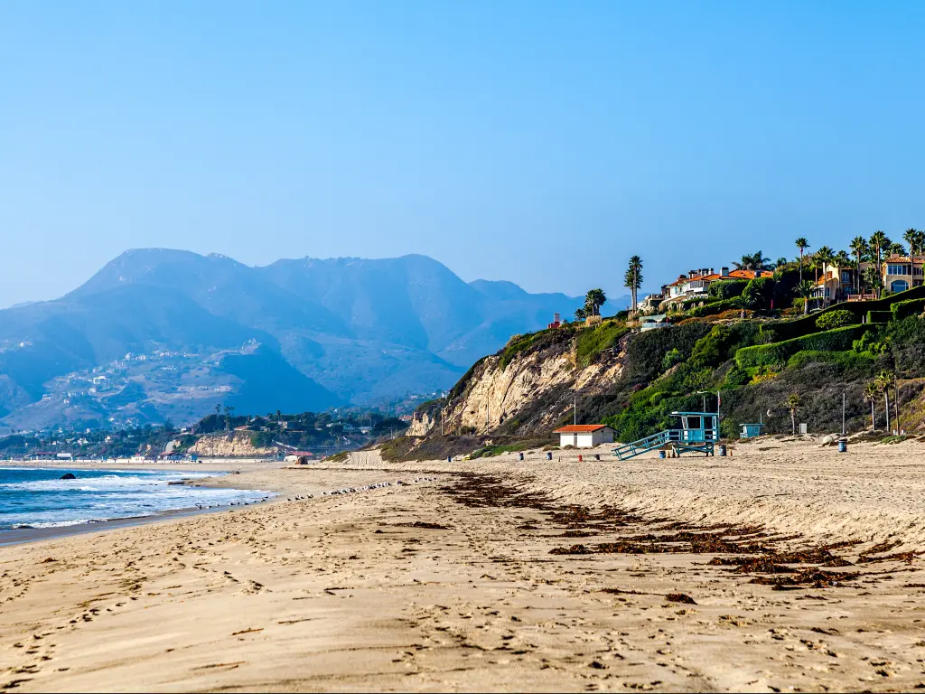 Malibu coastline with mountains in the background and mansions on a hill overlooking the beach.