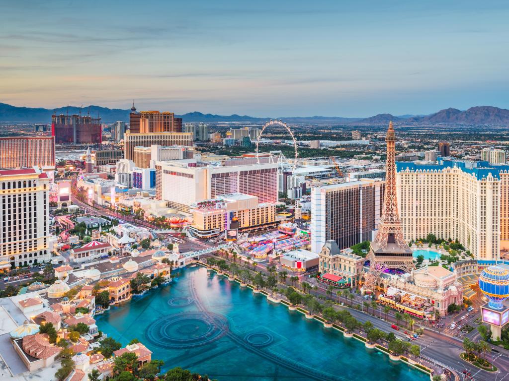 Las Vegas, Nevada, USA skyline over the strip at dusk with a huge swimming pool in the foreground and iconic buildings all around.