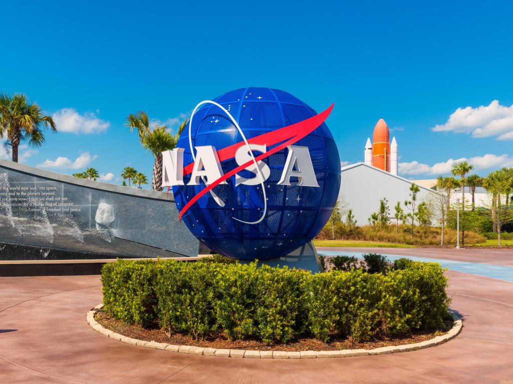 NASA Logo on Globe at Kennedy Space Center Visitor Complex in Cape Canaveral, Florida, USA. To the left is a painting visible of President John F. Kennedy.