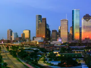 High rise buildings at night with dark blue sky and city lights of low rise buildings in foreground
