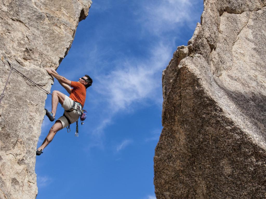 Rock climber clings to the edge of a challenging cliff in Joshua Tree National Park.