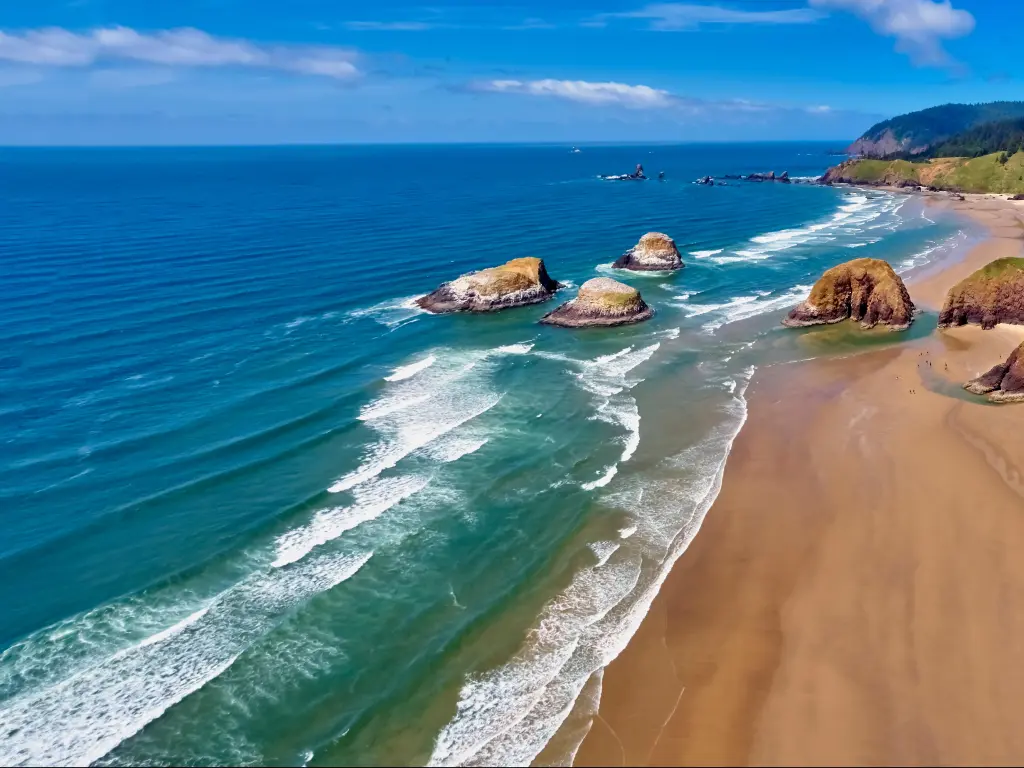 Cannon Beach, Oregon with an aerial shot of the beach looking towards Ecola State Park on a sunny blue sky day with a few rocks in the sand.