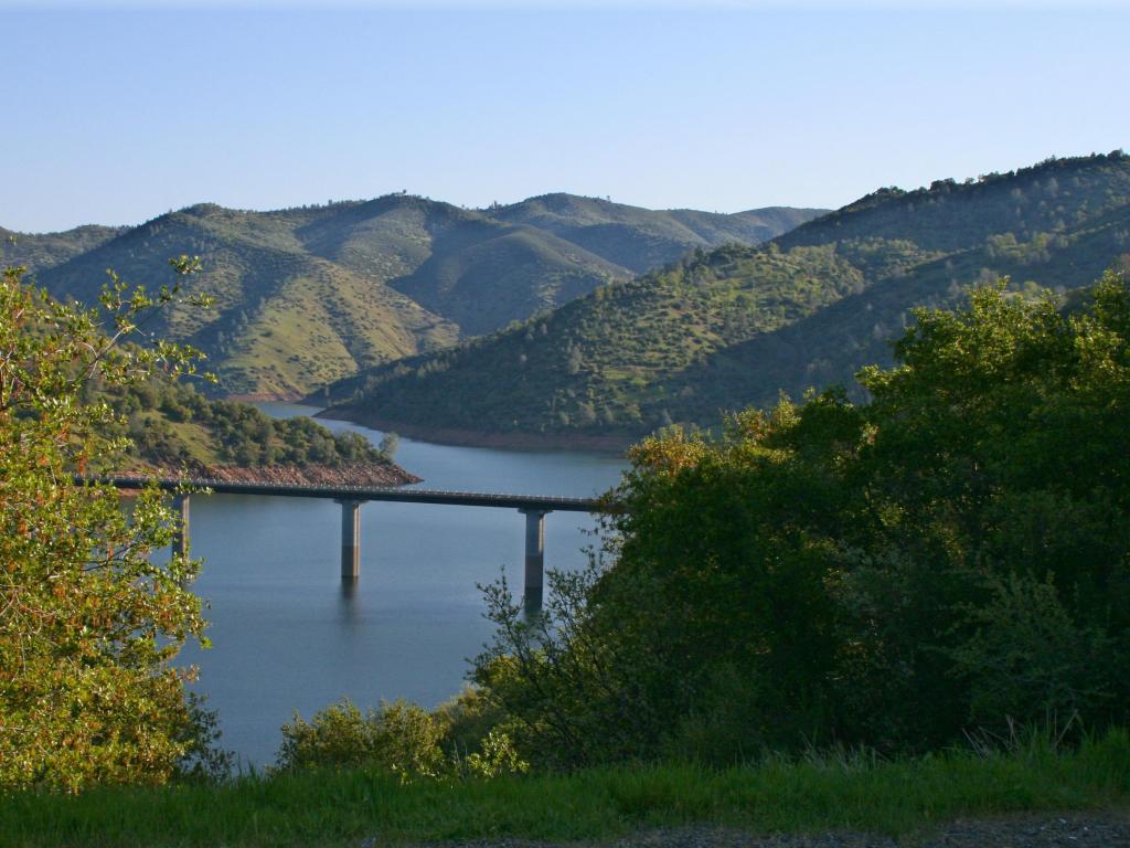 Aerial photo of the bridge spanning Don Pedro Reservoir, California, showing the green mountains surrounding the reservoir and lush vegetation