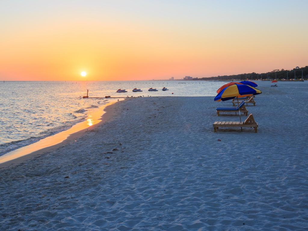 Biloxi beach, Mississippi at sunset overlooking the Gulf Coast shore with sunbeams and umbrellas on an empty beach.