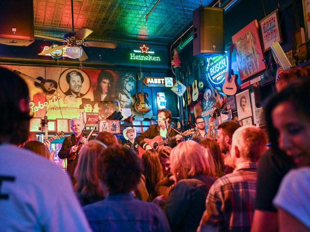 A busy bar in downtown Nashville, with people watching live music. Neon signs and music memorabilia line the walls