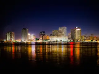 New Orleans, Louisiana, USA skyline at night with the city lights reflected in the dark water in the foreground.