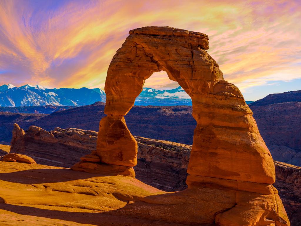 Arches National Park, Utah with the incredible arch rock in the foreground overlooking mountains and a beautiful sunset in the background.