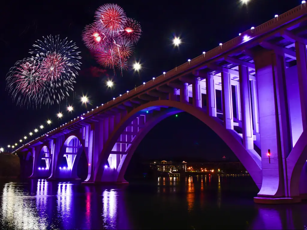 Bridge over wide river illuminated at night with large fireworks