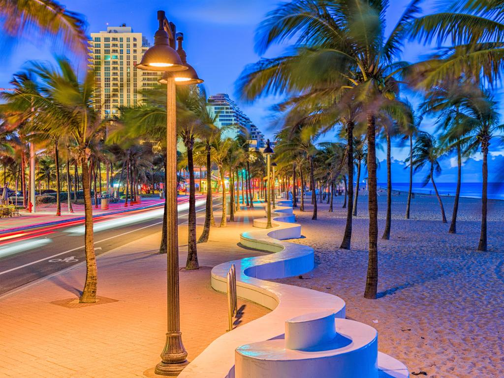 Fort Lauderdale, Florida, USA taken at the beach strip at dusk with palm trees lining the path and beach and the city in the distance. 