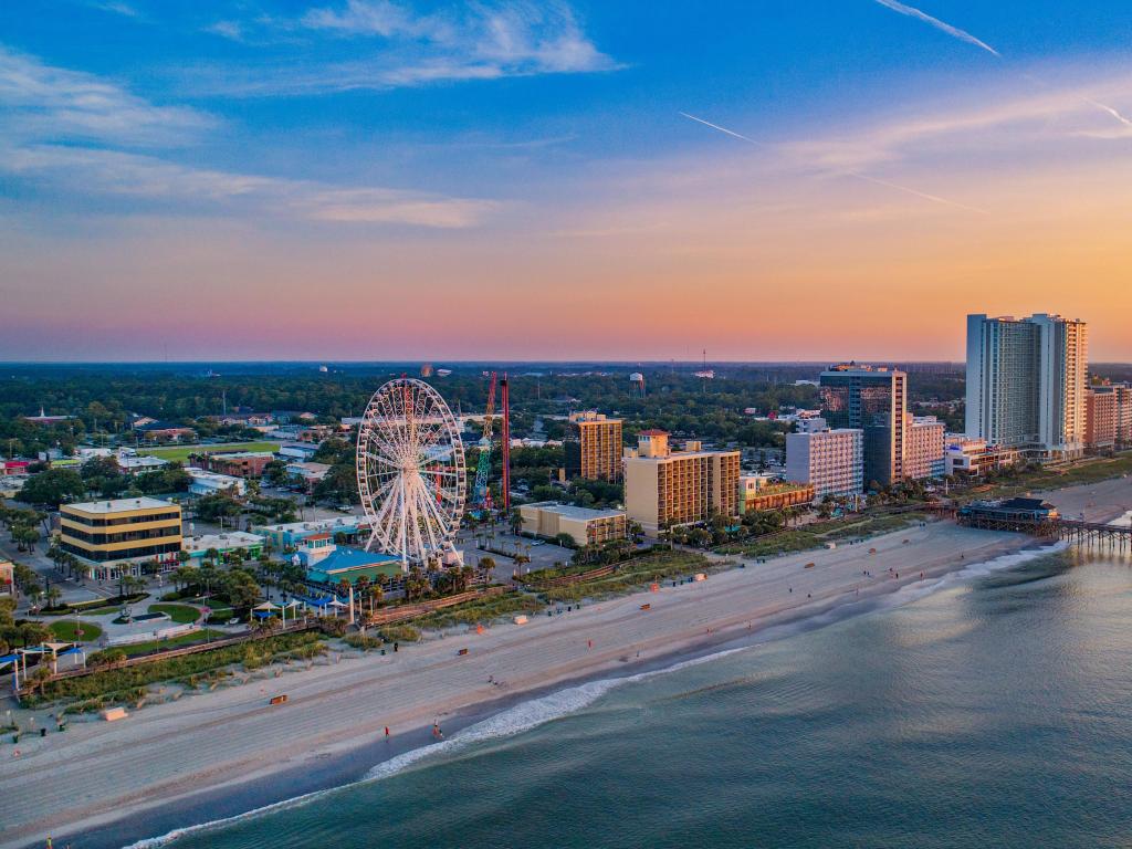 Myrtle Beach, South Carolina, USA with the pier and the edge of the city and beach and sea in the foreground taken as an drone aerial view at sunset.