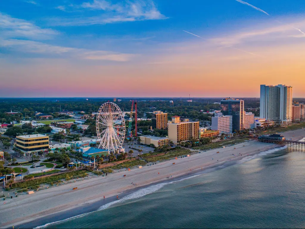 Myrtle Beach, South Carolina, USA with the pier and the edge of the city and beach and sea in the foreground taken as an drone aerial view at sunset.