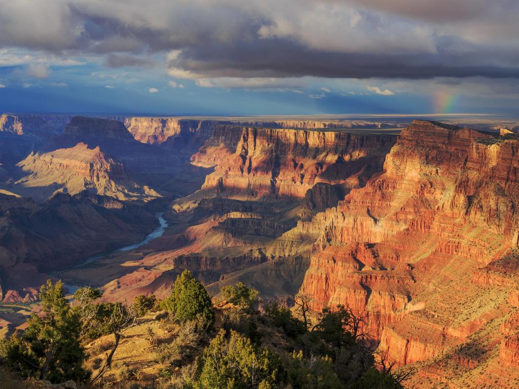 Grand Canyon, Arizona, USA with an incredible view from the South Rim, the river and trees and a distant  rainbow under a stormy sky.