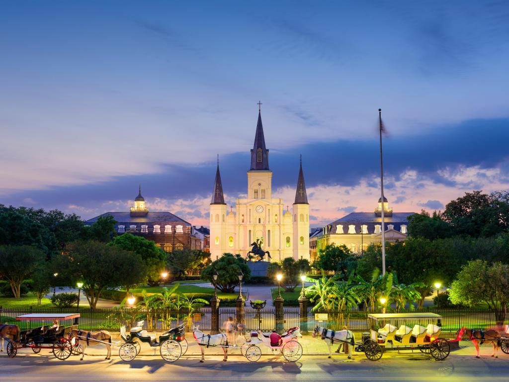 New Orleans, Louisiana, USA at St. Louis Cathedral and Jackson Square taken at night with horses and carts in the foreground.