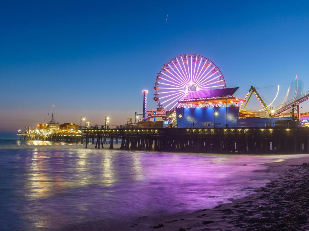 Santa Monica Pier illuminated with new LED lights at night with a reflection that can be seen on the waves.