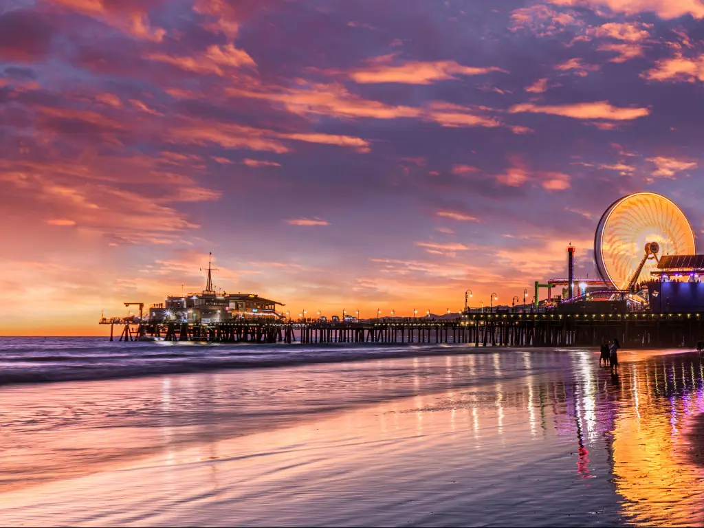 Santa Monica pier, California at sunset with the pier and fairground lit up and the sky reflecting in the sea.