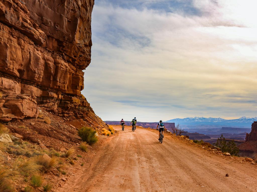 A group of cyclists ride around a bend in Cyclists in Canyonlands National Park, Utah, on a red rock dusty road