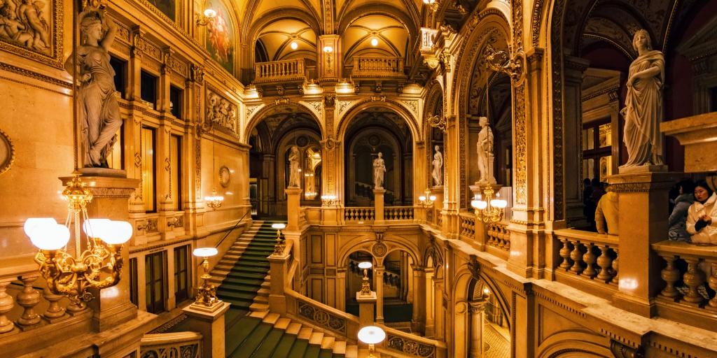 A curling staircase inside the Vienna State Opera House, Austria, with a green carpet and statues around the edges