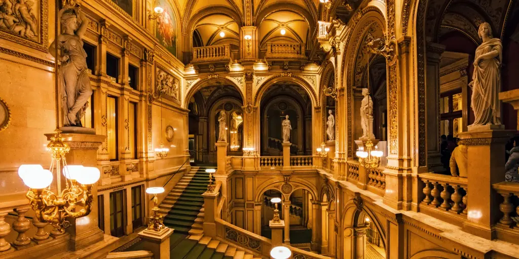 A curling staircase inside the Vienna State Opera House, Austria, with a green carpet and statues around the edges