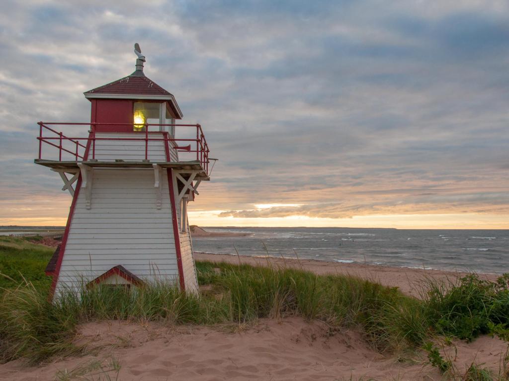 Covehead Lighthouse, Stanhope, Prince Edward Island, Canada taken at sunset with colorful clouds behind the lighthouse and sandy dunes surrounding it.