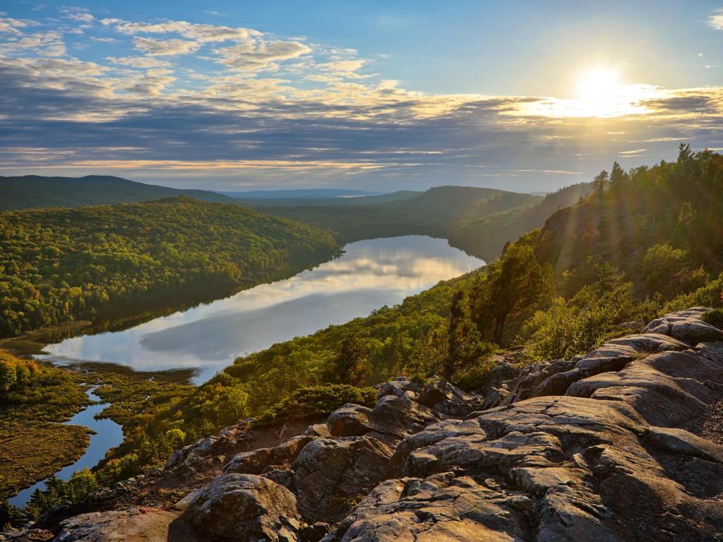 Porcupine Mountains State park in Upper Michigan, USA with a view of the Lake of the Clouds at sunset with rocks and trees in the foreground.