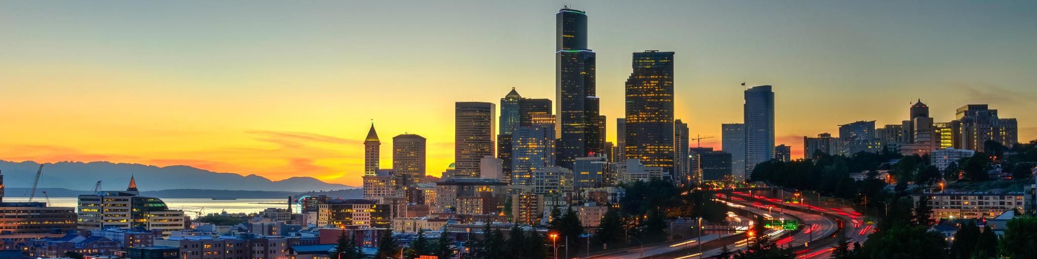 The view from Rizal Park of Seattle skyline during sunset with highway traffic motion.