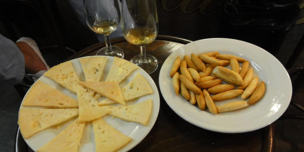 Slices of cheese and breadsticks and two wine glasses on a table at a tapas bar