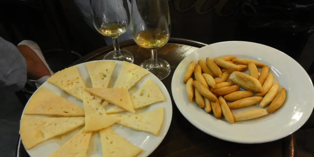 Slices of cheese and breadsticks and two wine glasses on a table at a tapas bar