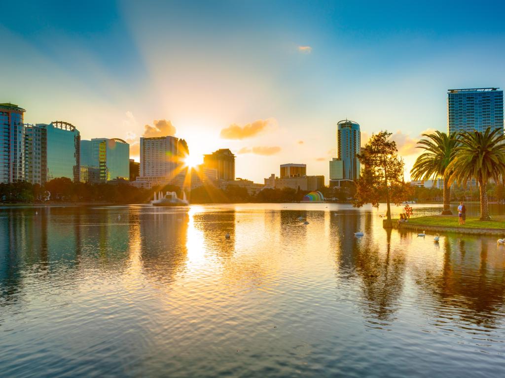 Setting sun illuminates high rise buildings set around a lake with palm trees
