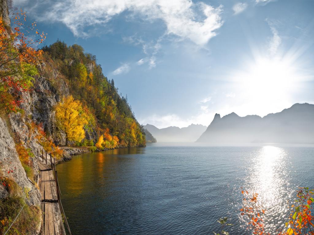 A walking trail next to a lake in Austria surrounded by colourful autumn leaves and a glittering lake