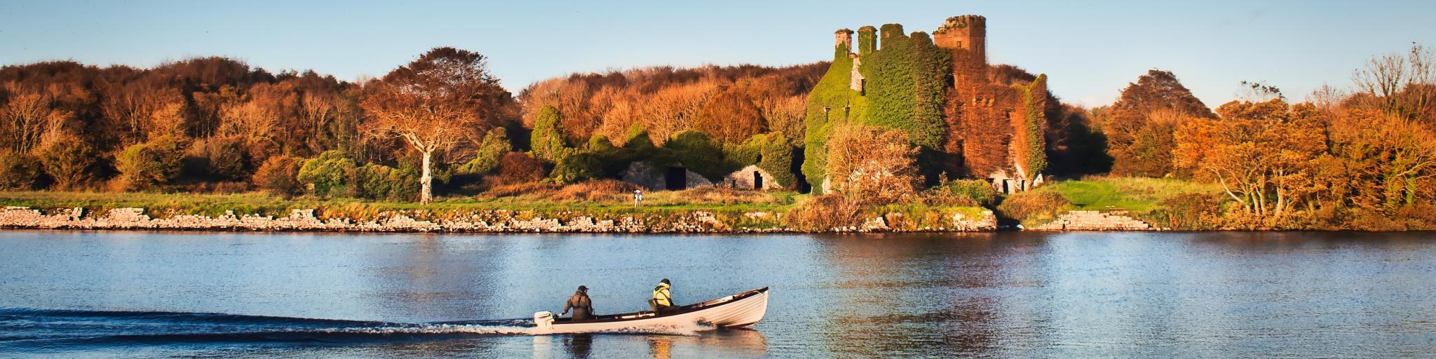 Beautiful scenery of Menlo castle surrounded by a autumn colored trees and boat passing by in Corrib river at Galway, Ireland